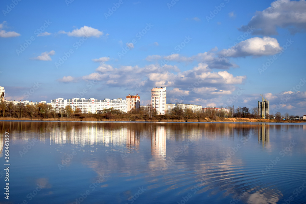 on the shore of the lake is a city that is reflected along with the sky and clouds in the water