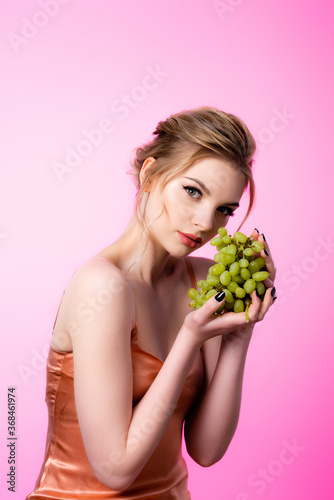 elegant beautiful blonde woman holding green grapes isolated on pink