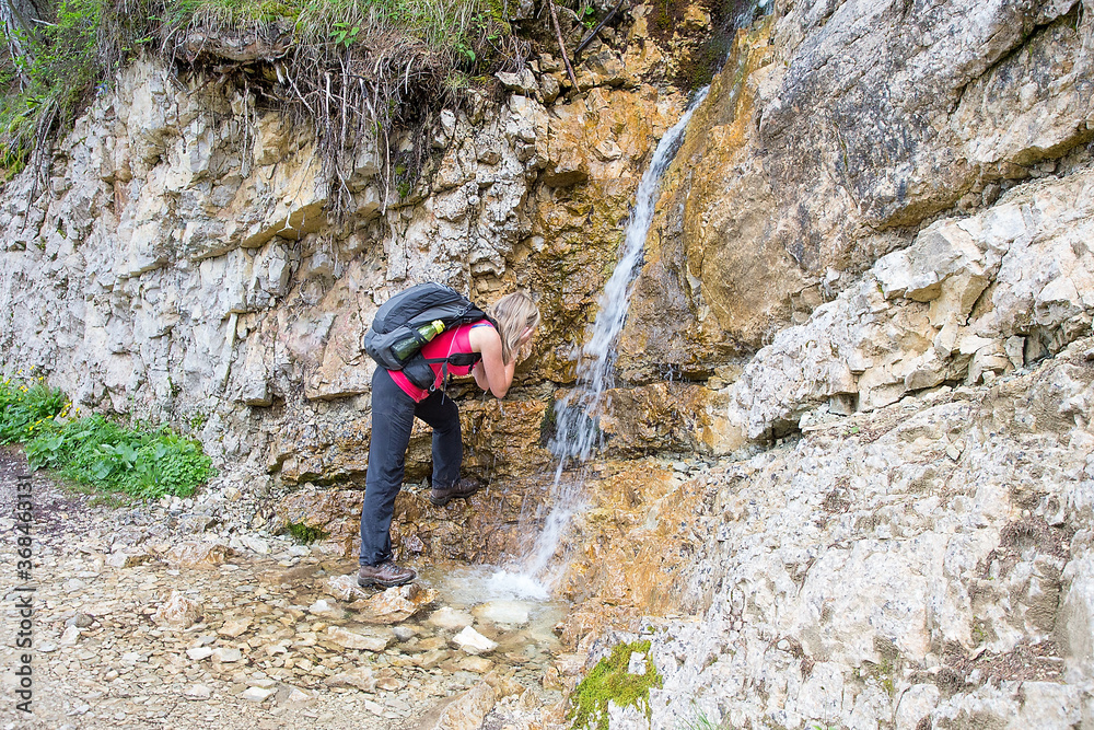 Adult hiker drinks water at the spring in Dolomites, Lago Sorapis, Italy