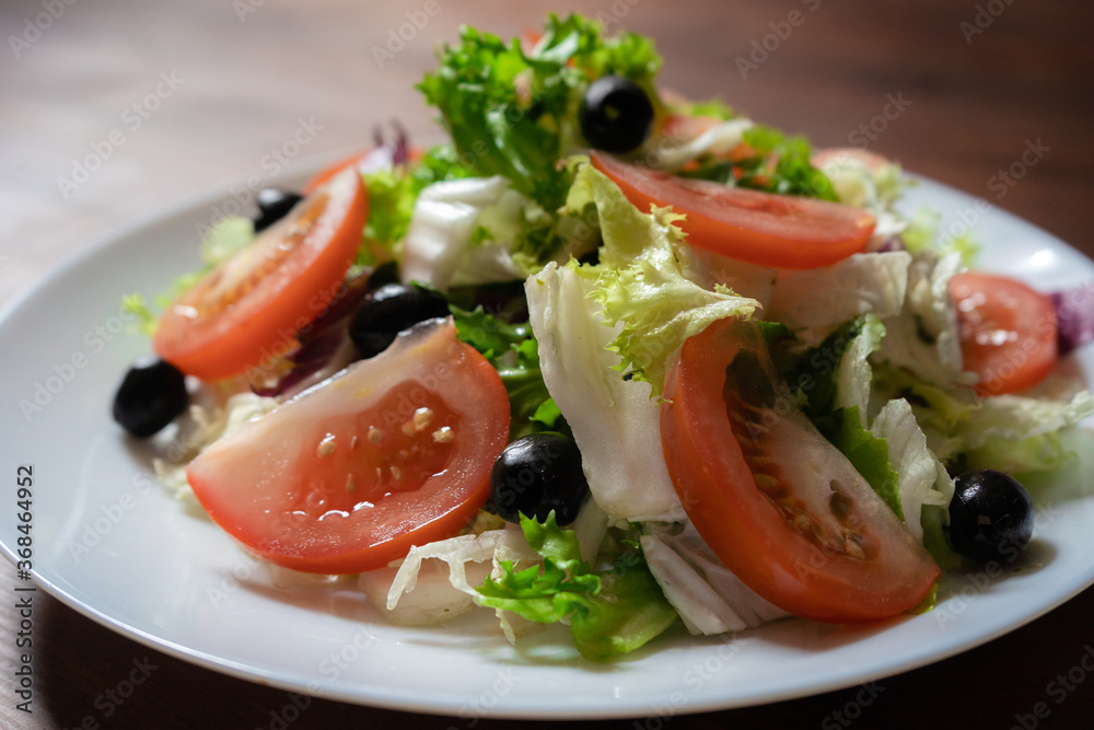 Healthy food concept. Vegetable salad with green lettuce, red tomatoes and black olives. Colorful natural vitamin appetizer. Fresh spring refreshment on white plate. Close up shot.