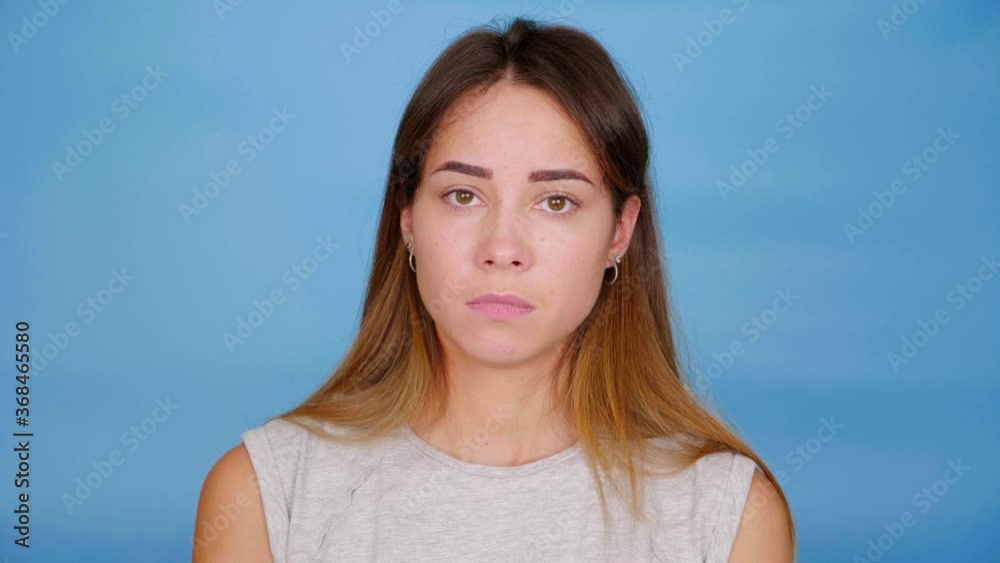Sad woman in gray t-shirt nods head and says yes on blue background with copy space. 4K slow motion footage