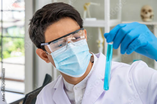 Asian male researcher scientist holding and examine test tube filled with blue liquid chemical in laboratory