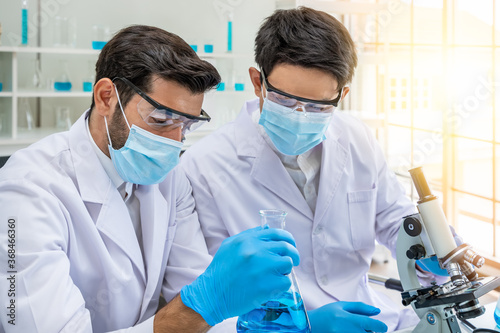 Two male Asian and Arab researcher scientists working in laboratory, conducting study biohazard substance with scientific equipment and microscope