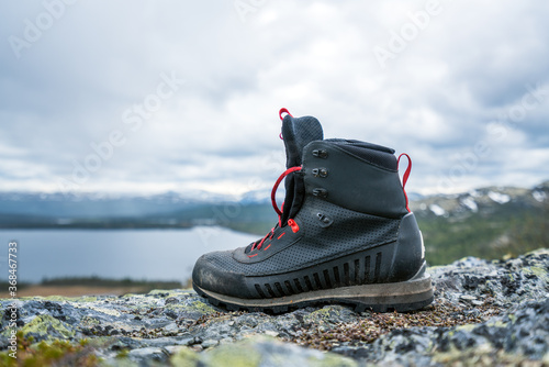 Black hiking, trekking boots outdoors in the wilderness during hike with lake and landscape scenery in the background.