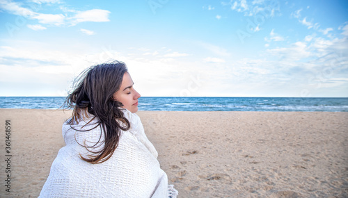 A young woman by the sea is covered with a blanket