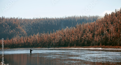 Profile of a fisherman on the background of the taiga river in autumn.