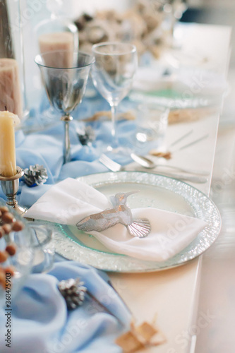 Festive table setting for Christmas and New Year in blue colors. Hummingbird figurine decorates plate.