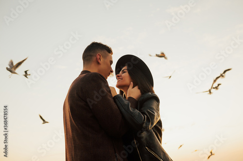 Obraz na płótnie Happy young romantic couple hugging and looks at each other with love. Young couple sharing happy and love mood on the beach with flying seagulls on background. w salonie