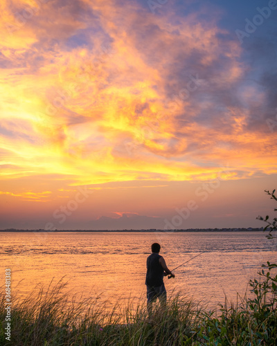 Silhouette of a man fishing under a warm vibrant summer sunset. Long Island New York. 