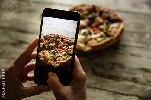 Female hands holding a smartphone and taking photo of a delivered pizza.