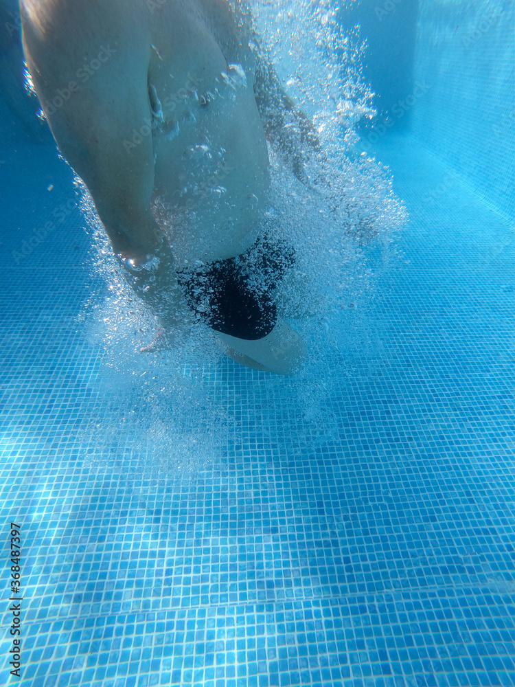 Swimmer coming out of the blue pool surrounded by bubbles in the water. Vertical photo with negative space.