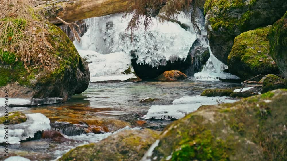 River with ice with waterfalls in a green forest through blurred stones River with ice with waterfalls in a green forest through blurred stones