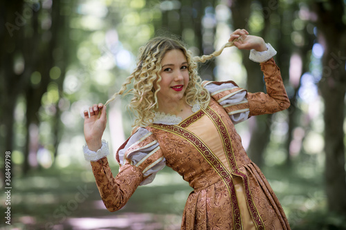 Young woman with white curly hair dressed in an medieval dress among trees