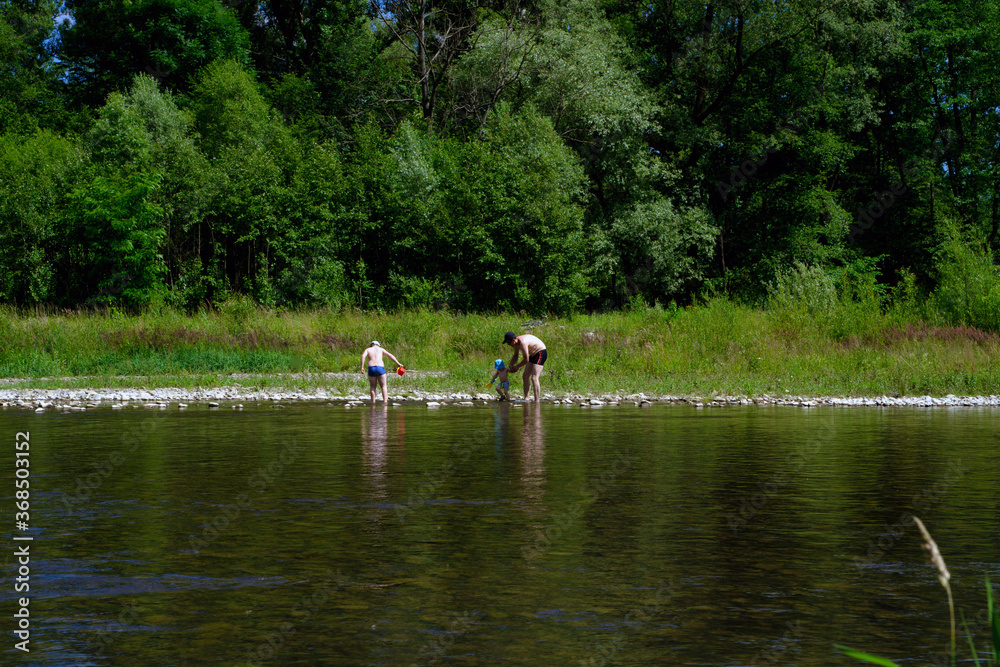 Fototapeta premium Bielsko Biala, Poland - July 04, 2020: A family consists of Father and two sons at the bay of Sola river near Wieprz