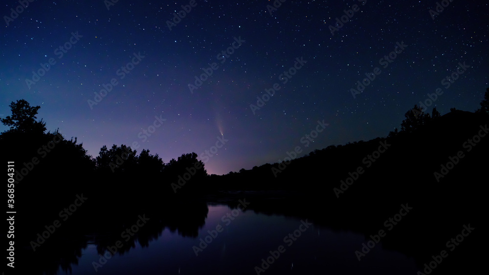 Comet NEOWISE in the night sky. C / 2020 F3 retrograde comet and tail with a near-parabolic orbit at sunset. Comet under the starry sky, in the evening, between the stars. River and space background.