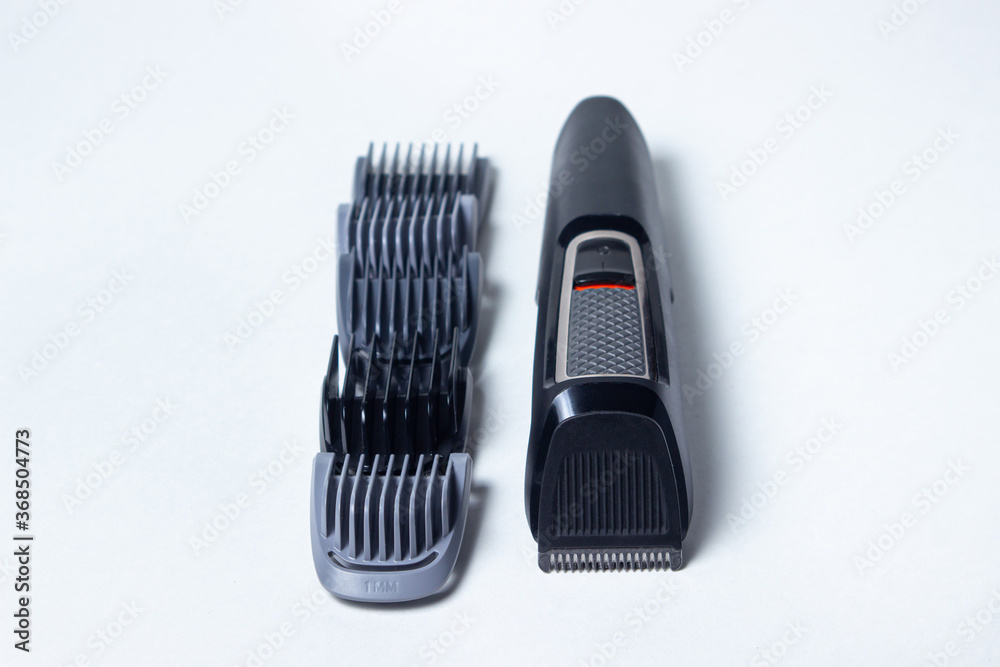Beard trimmer on a white background. Different sized attachments are placed next to the trimmer. Beard care. Male style