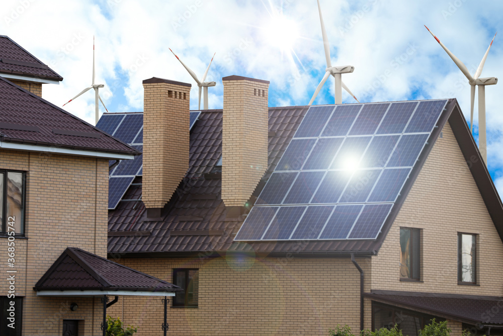 Fototapeta premium Wind turbines near house with installed solar panels on roof. Alternative energy source