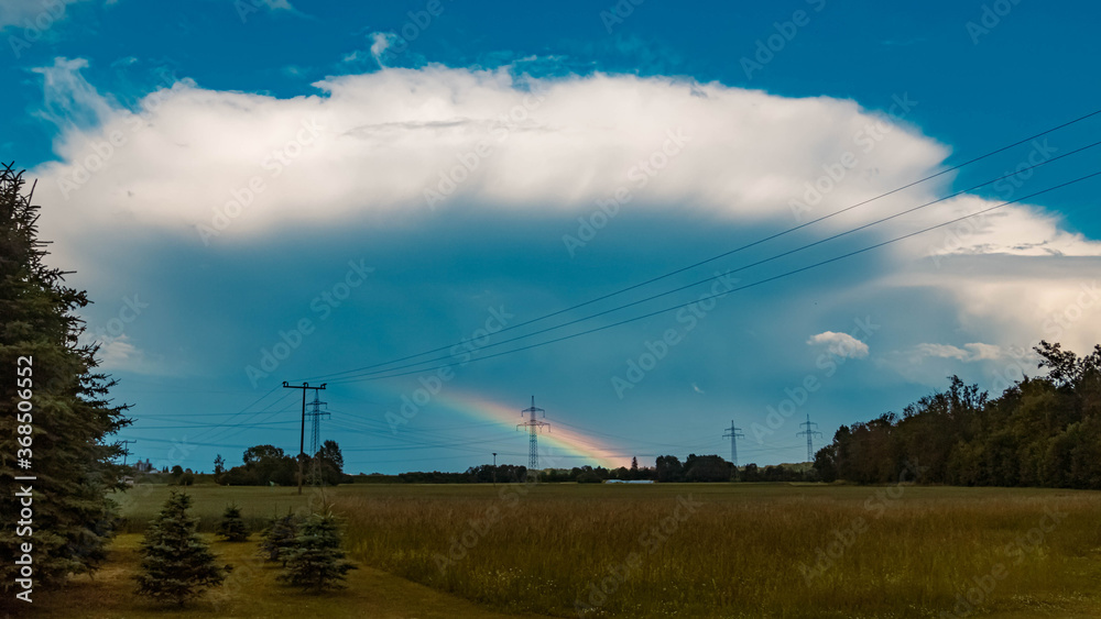 Beautiful rainbow with powerlines and a big storm cloud near Tabertshausen, Bavaria, Germany Beautiful rainbow with powerlines and a big storm cloud near Tabertshausen, Bavaria, Germany