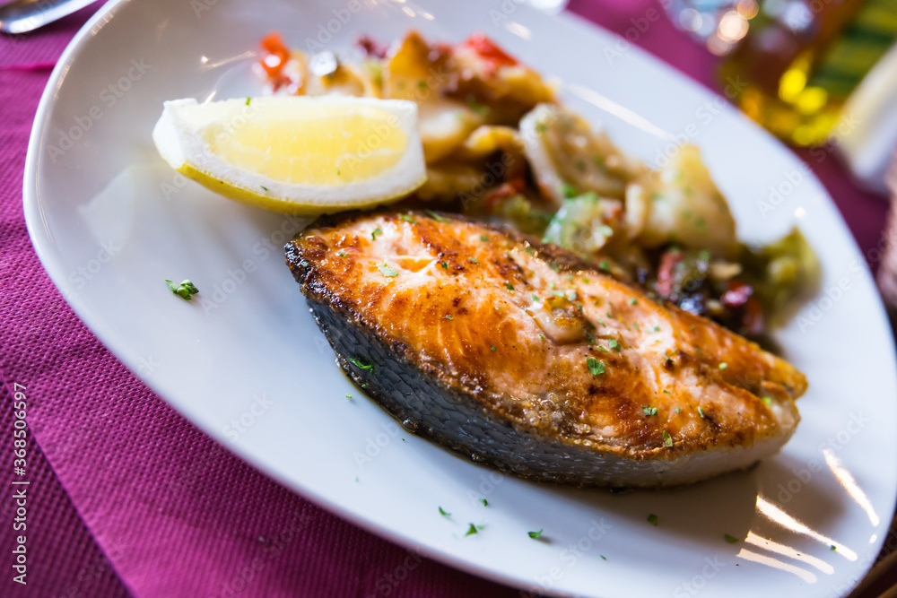 delicious salmon steak with potato garnish with slice of lemon on white plate in restaurant delicious salmon steak with potato garnish with slice of lemon on white plate in restaurant
