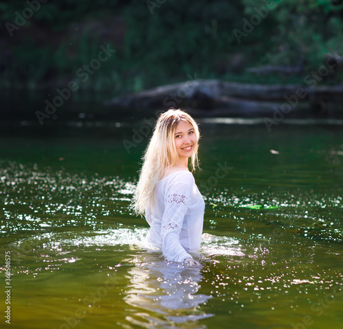 Young white woman with long blondy hair in a river in a forest in summer