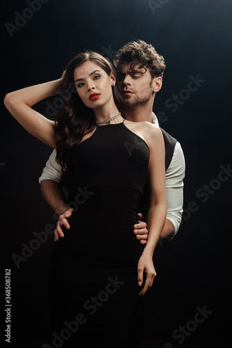 Handsome man embracing sexy woman with red lips on black background