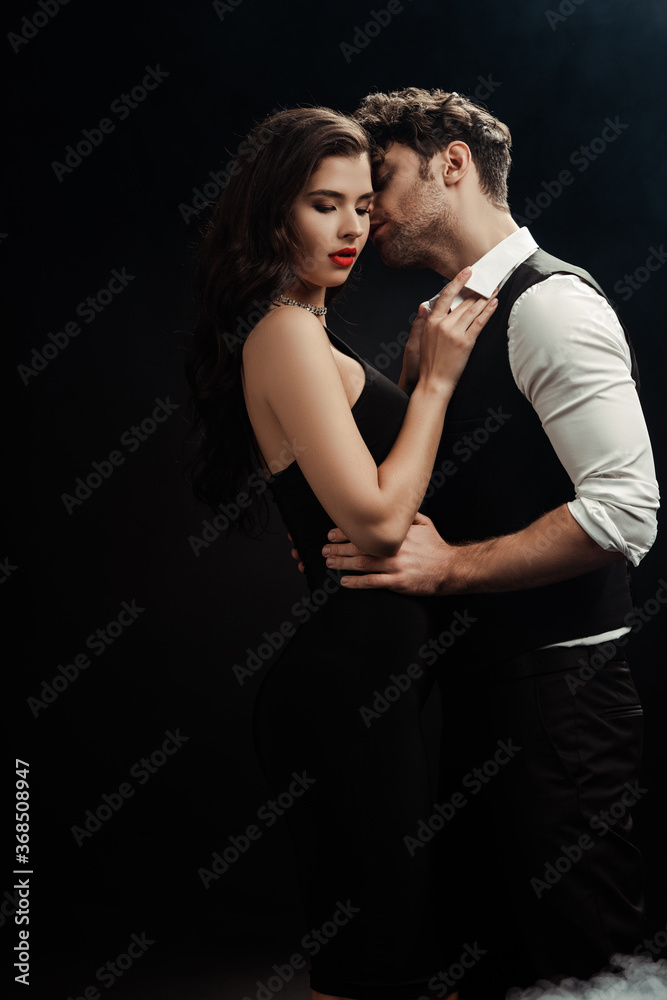 Side view of handsome man kissing sexy woman on black background
