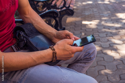 man using a smart phone sitting on a bench in a city street.close up