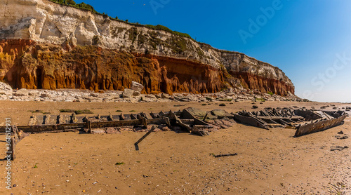 A carcass of a shipwreck on Old Hunstanton Beach resting beneath the white, red and orange stratified cliffs in UK photo