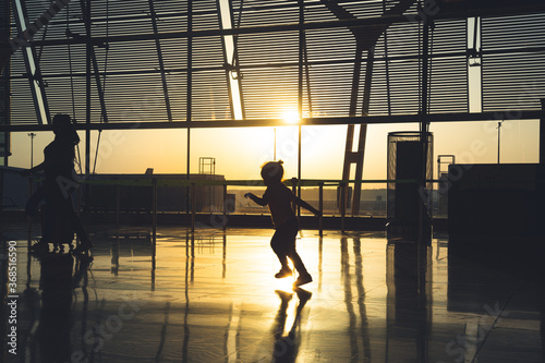 silhouette of an unrecognizable child running through the airport terminal at sunrise.