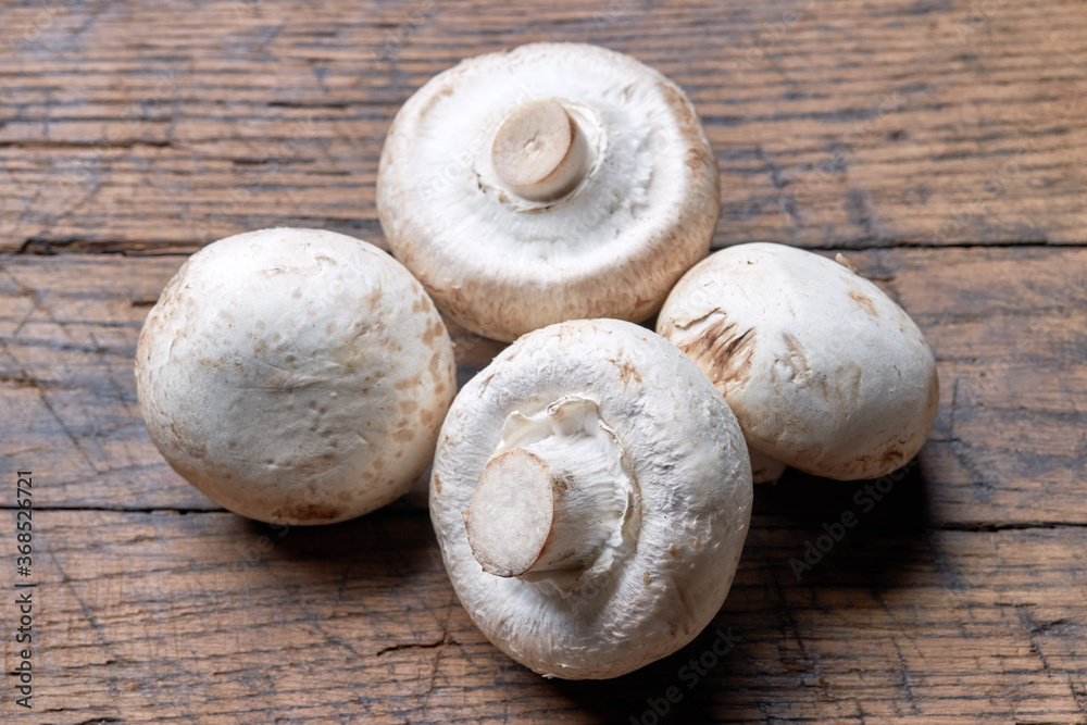 stack of raw fresh champignon mushrooms close up on a wooden rustic background