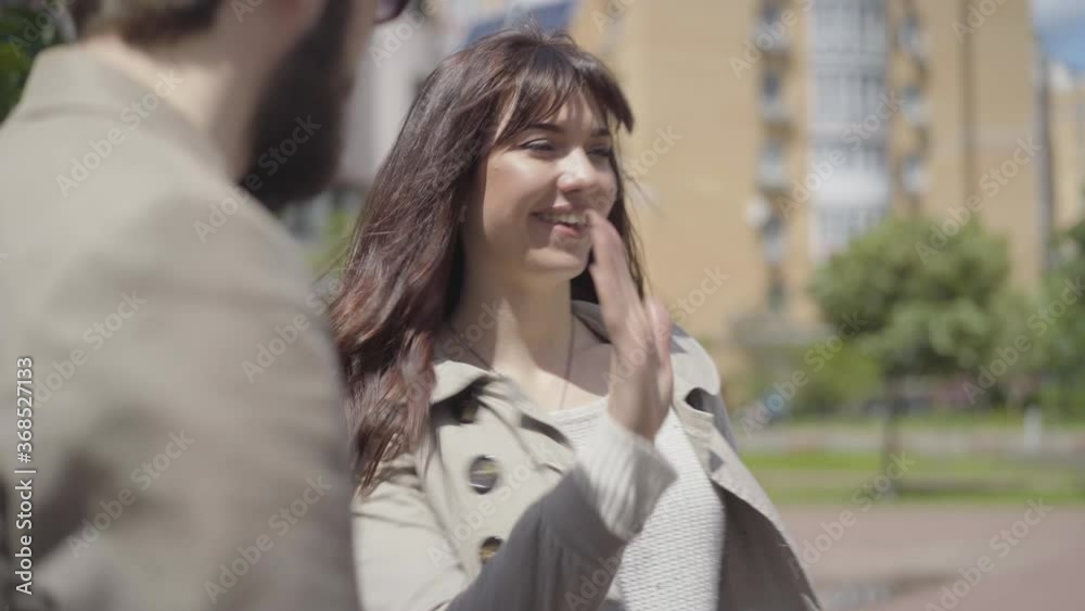 Bearded Caucasian man and smiling brunette woman using smartphone as meeting friend on sunny city street. Portrait of positive friends greeting each other and leaving. Bearded Caucasian man and smiling brunette woman using smartphone as meeting friend on sunny city street. Portrait of positive friends greeting each other and leaving.
