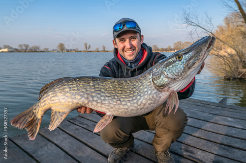 Success pike fishing. Happy fisherman with big fish trophy in hands