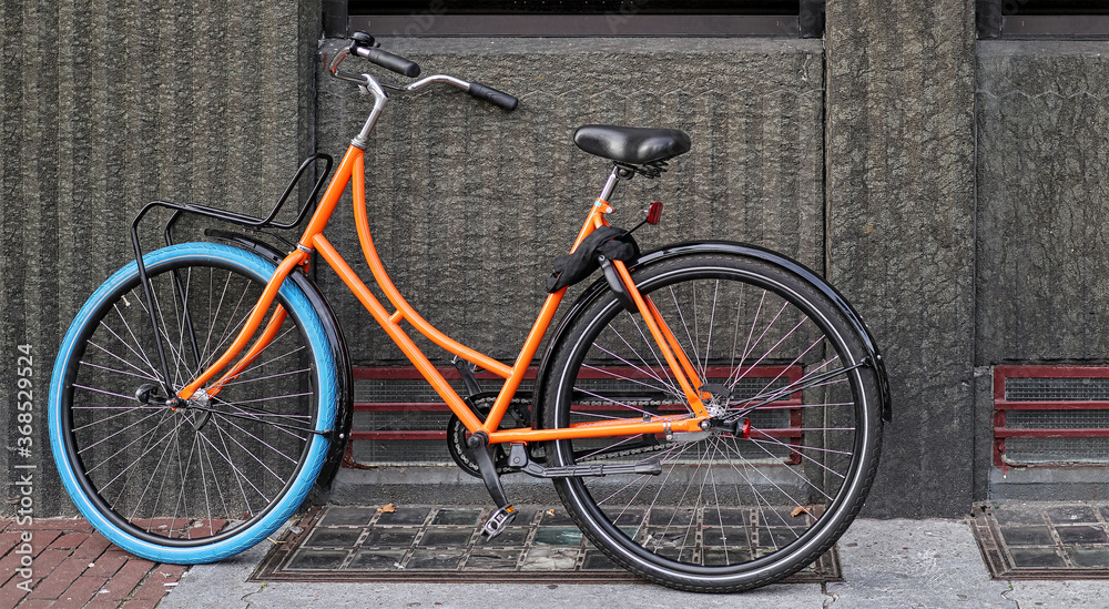 old vintage bicycle in orange and blue colors parked on an old sidewalk wall