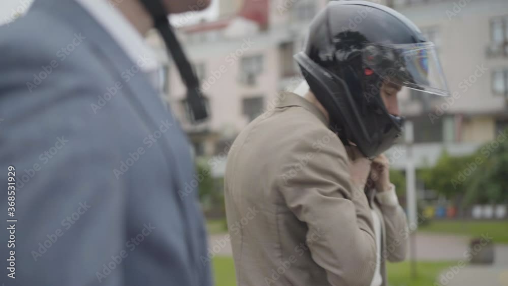 Confident Caucasian bikers putting on helmets on city street. Portrait of young men and woman preparing for racing on cloudy summer day. Active lifestyle concept. Confident Caucasian bikers putting on helmets on city street. Portrait of young men and woman preparing for racing on cloudy summer day. Active lifestyle concept.