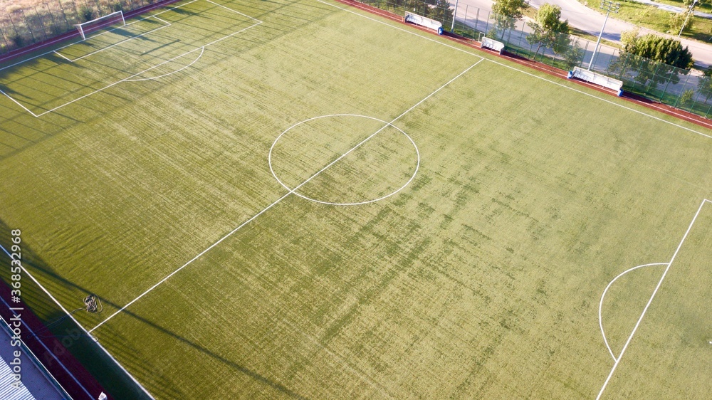 Aerial view of grass football field near the forest, road and buildings at the sunset. the camera moves towards the midfield