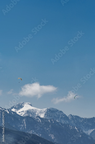 Two paragliders are flying over a mountains in Bavaria on background of blue sky with clouds in spring sunny day. Vertical wallpaper