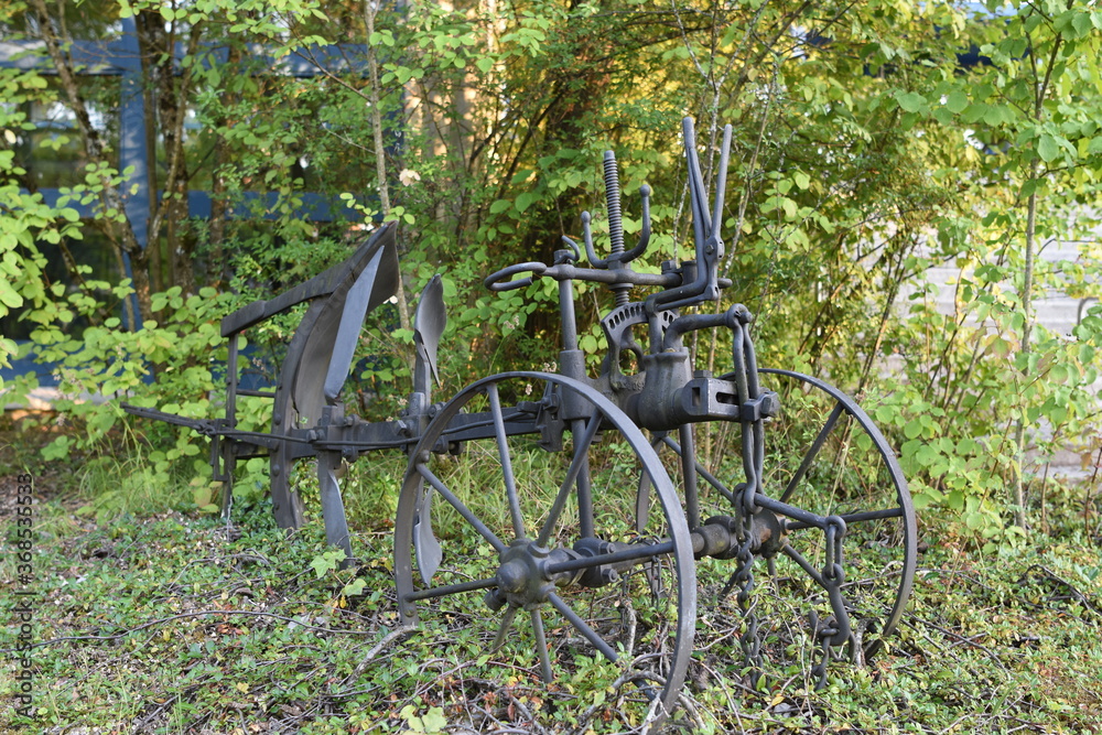 Old restored iron black farm plow exposed in the grass patch in front of secondary school in Switzerland

