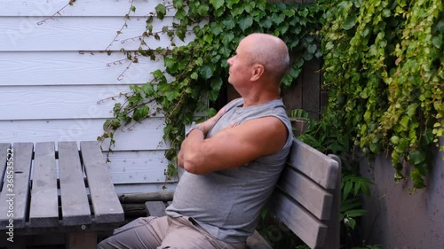 bald old man sits on a wooden bench at a table on the terrace and thinks, concept of age, reflections on life
