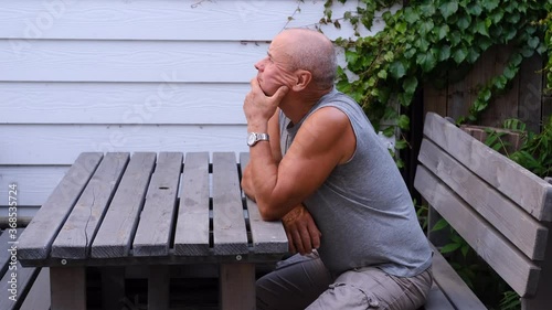 bald old man sits on a wooden bench at a table on the terrace and thinks, concept of age, reflections on life