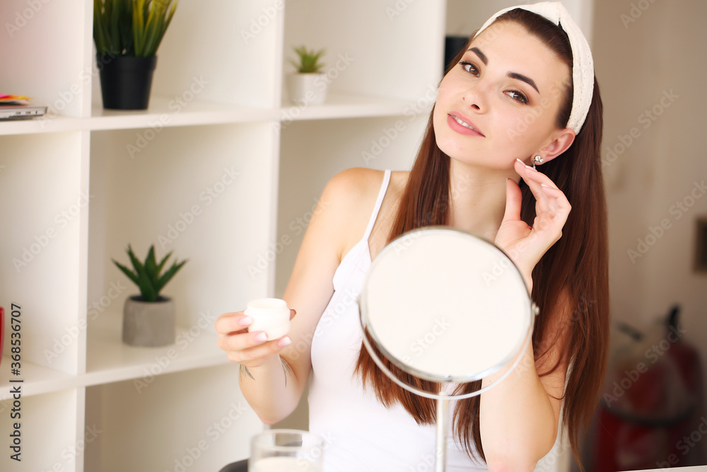 beauty, skincare young woman applying face cream and looking in mirror in home bathroom. beauty, skincare young woman applying face cream and looking in mirror in home bathroom.