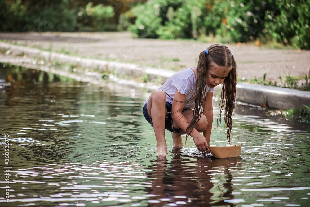Cute happy kids playing with paper boat in the puddles after warm summer rain, lifestyle outdoor
