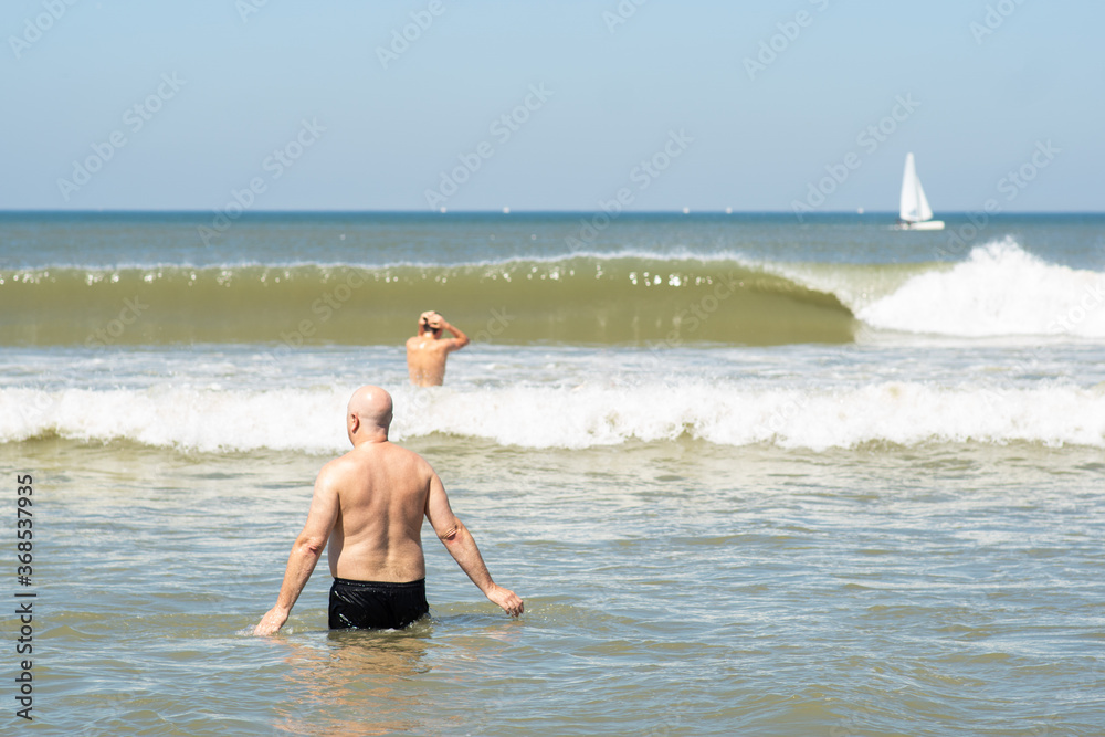 People swimming in the sea water, towards big waves - concept of drowning danger and safe summer at the beach. No recognizable people.