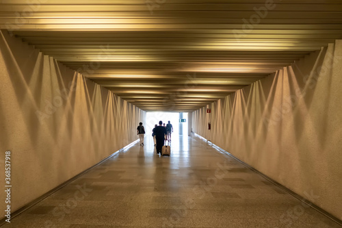 people walking down an airport corridor with yellow walls with a set of lights on the ceiling and walls