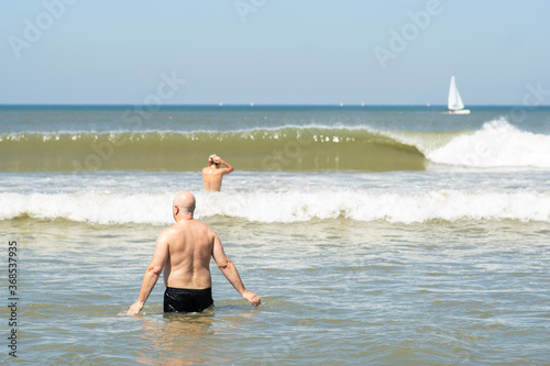 Obraz na płótnie People swimming in the sea water, towards big waves - concept of drowning danger and safe summer at the beach. No recognizable people. w salonie