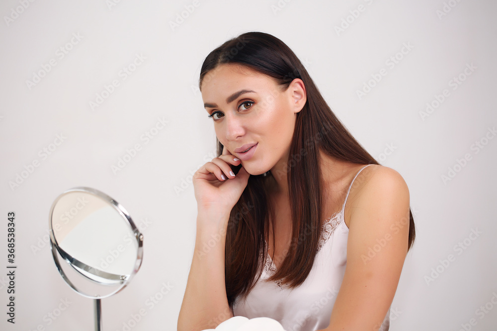beauty, skin care and people concept - smiling young woman in hairband touching her face and looking to mirror at home bathroom beauty, skin care and people concept - smiling young woman in hairband touching her face and looking to mirror at home bathroom