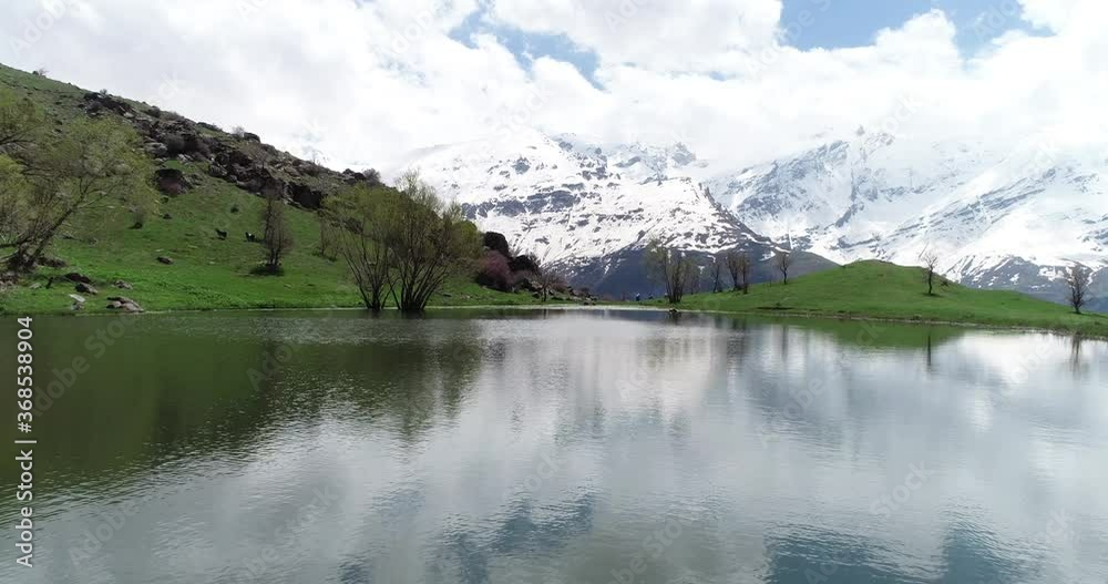 Aerial view of snowy mountain, green field and lake with cloudy sky. Aerial view of snowy mountain, green field and lake with cloudy sky.