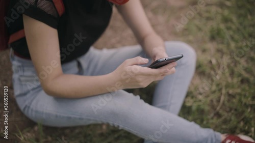 High angle view of a young woman sitting on the grass in the park. Close-up of the hands holding a smartphone. Soft-focus dreamy look. 