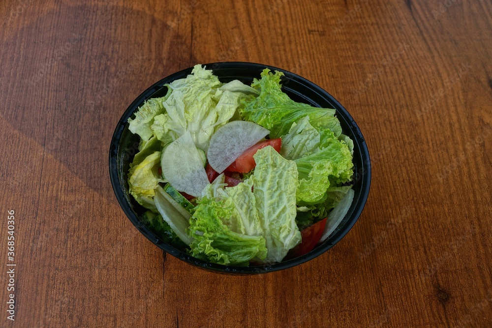 food from pieces of raw vegetables in a black plastic plate stands on a brown wooden table food from pieces of raw vegetables in a black plastic plate stands on a brown wooden table