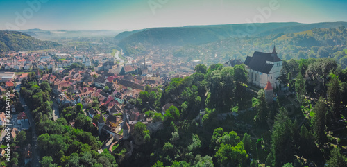 Drone aerial morning panorama of Citadel and Biserica din Deal rising above Sighisoara in Romania. View towards the beautiful  old town.