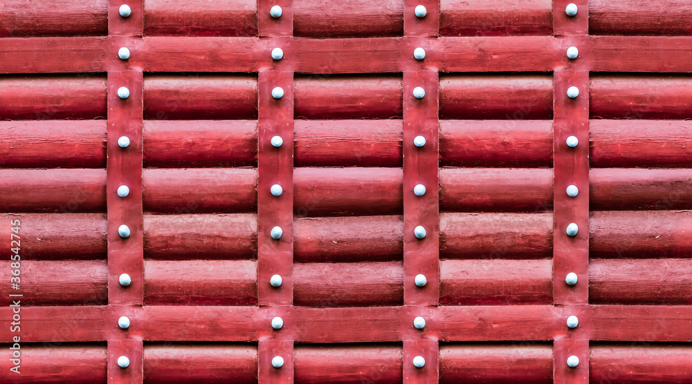 red wooden pattern, the wall is made of logs with iron vertical iron stripes and rivets red wooden pattern, the wall is made of logs with iron vertical iron stripes and rivets
